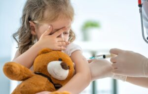 picture of doctor administering a shot to a young girl holding a stuffed bear
