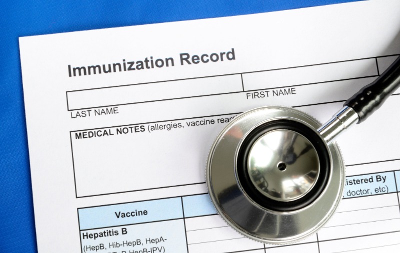 A blank "Immunization Record" form with fields for name and medical notes, partially covered by a stethoscope's chest piece, on a blue background.