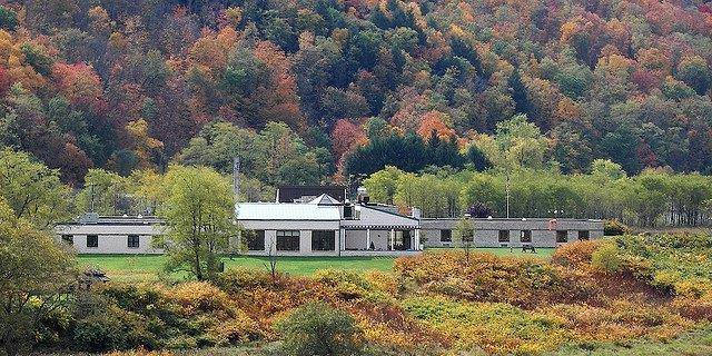 A long, single-story medical center building with a peaked roof section, surrounded by autumn foliage and forested hills in the background.