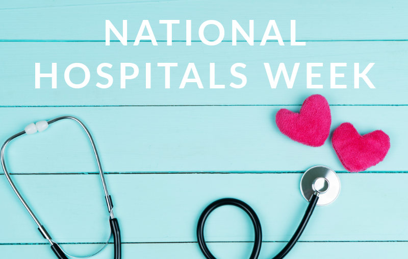Text reading "National Hospitals Week" in white letters over a light teal wood-plank background, with a black stethoscope and two pink fabric hearts arranged below.